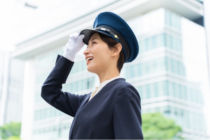 笑顔で敬礼する女性タクシードライバー。制服と制帽を着用し、近代的なビル街を背景にしたプロフェッショナルな姿。