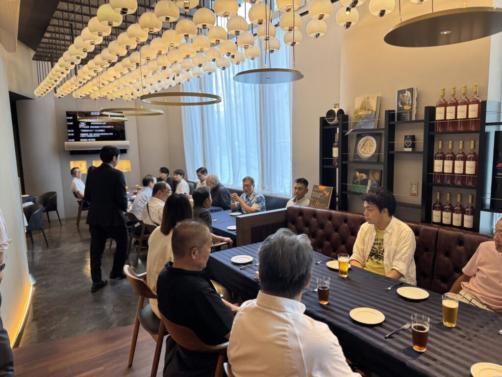 懇親会の会場で談笑する参加者たち。テーブルにはビールやドリンクが並び、和やかな雰囲気の交流イベントが行われている様子。

