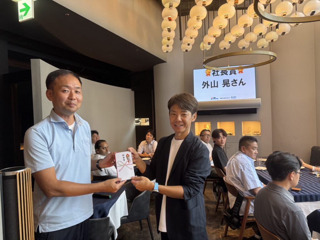 国際交通株式会社の懇親会で表彰を受ける社員。代表者から記念品を受け取り、拍手と笑顔に包まれた瞬間。
