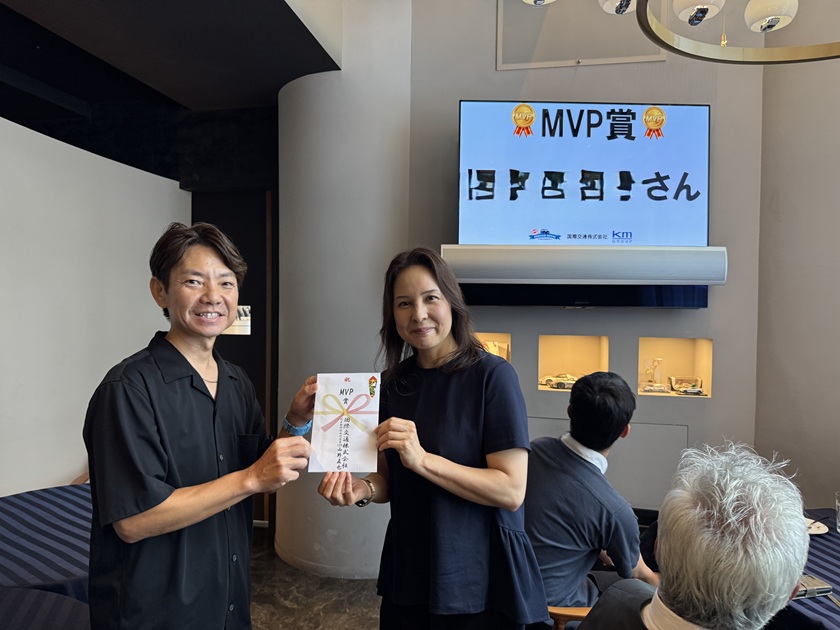 国際交通株式会社の社内表彰式で、MVP賞を受賞した社員が表彰者と賞状を掲げて記念撮影している写真