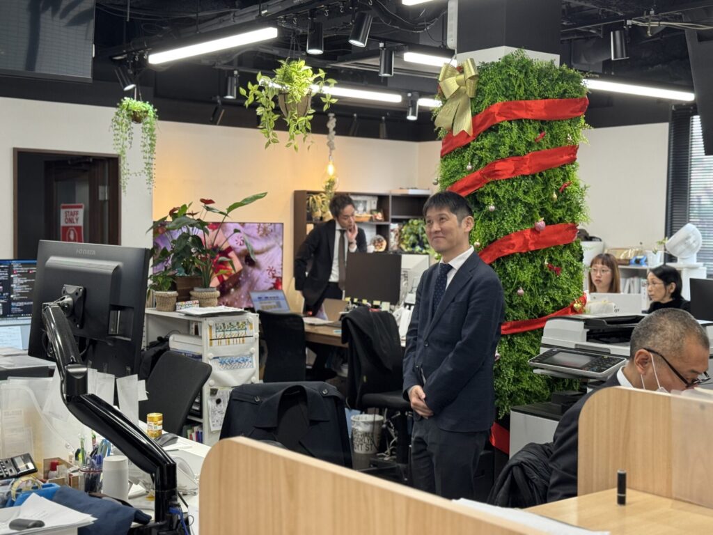 国際交通株式会社のオフィスで、クリスマス仕様に飾られたグリーン柱と働く社員の様子を写した写真